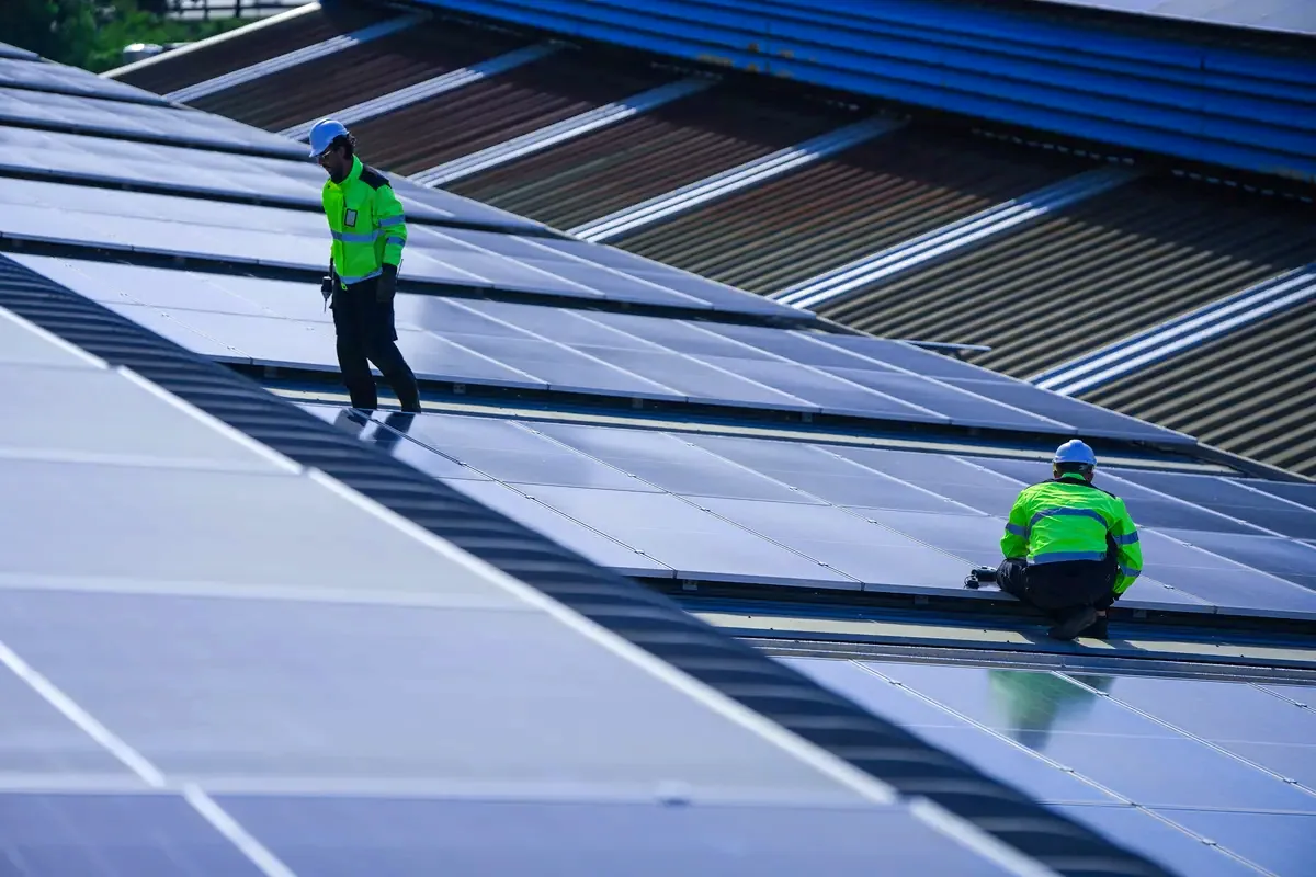 Dos operarios instalando paneles solares sobre la cubierta de una nave industrial en Hospitalet